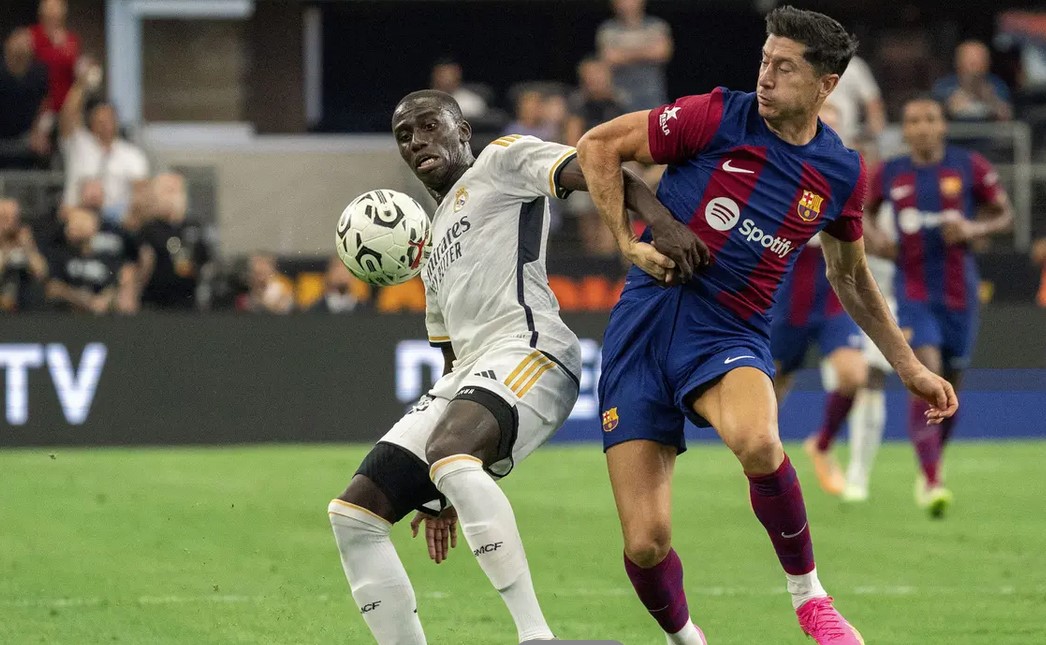 Bek Real Madrid, Ferland Mendy (kiri) berebut bola dengan striker Barcelona, Robert Lewandowski pada laga pramusim Soccer Champions Tour 2023 di AT&T Stadium, Arlington, Texas, Minggu (30/7/2023) dini hari WIB. (AP Photo/Jeffrey McWhorter)/Hibata.id