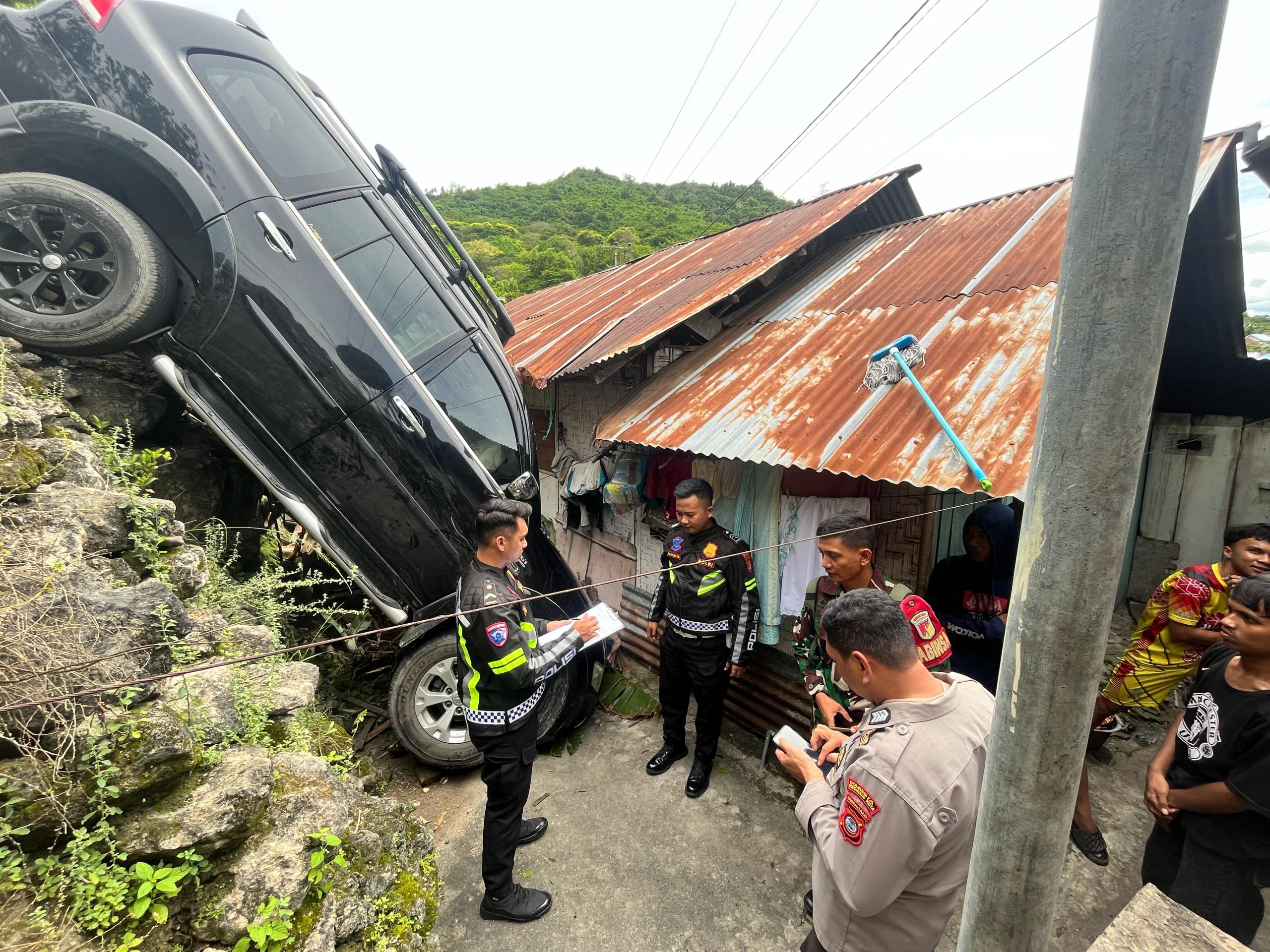 Sebuah mobil SUV berwarna hitam melaju tidak stabil. Sebelum akhirnya menghantam dua tiang listrik dan terjun ke jurang kecil belakang rumah warga/Hibata.id